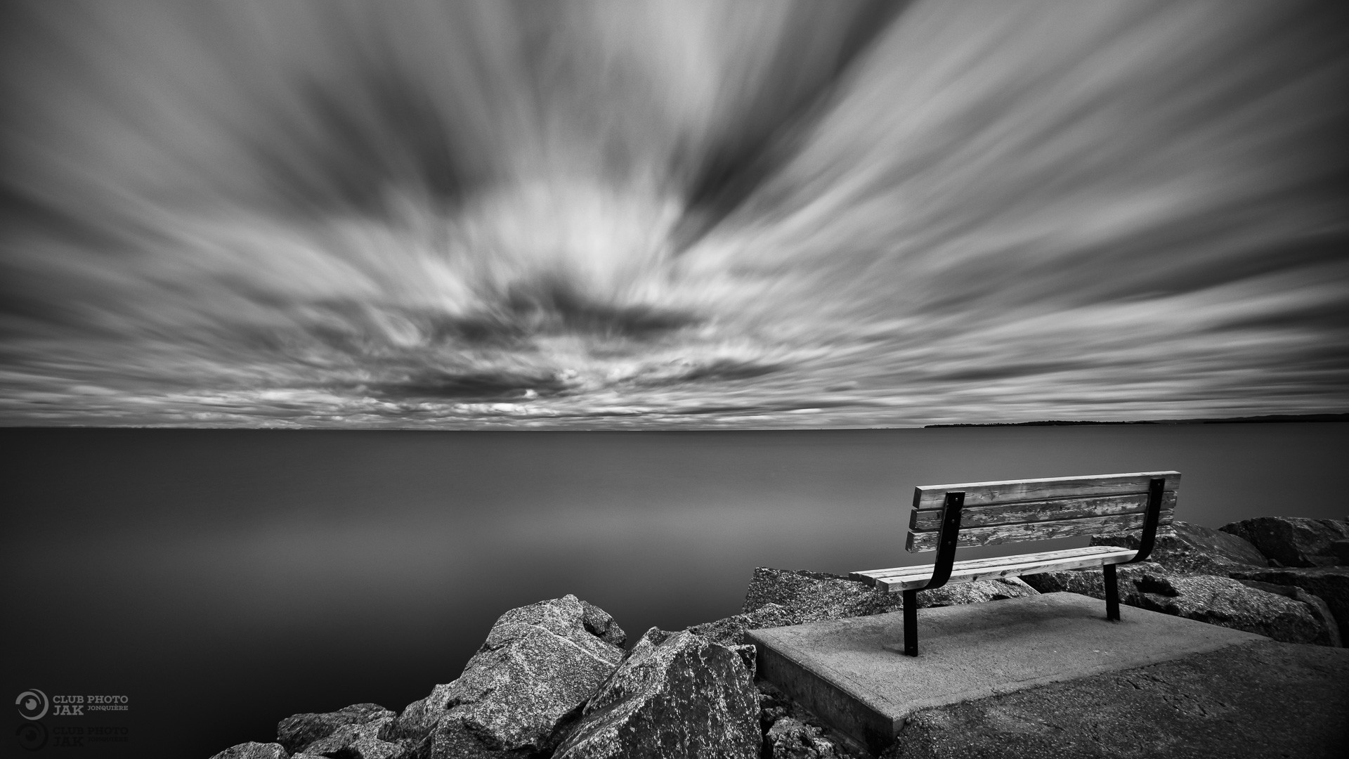 Banc au bord de l'eau avec un ciel mouvementé